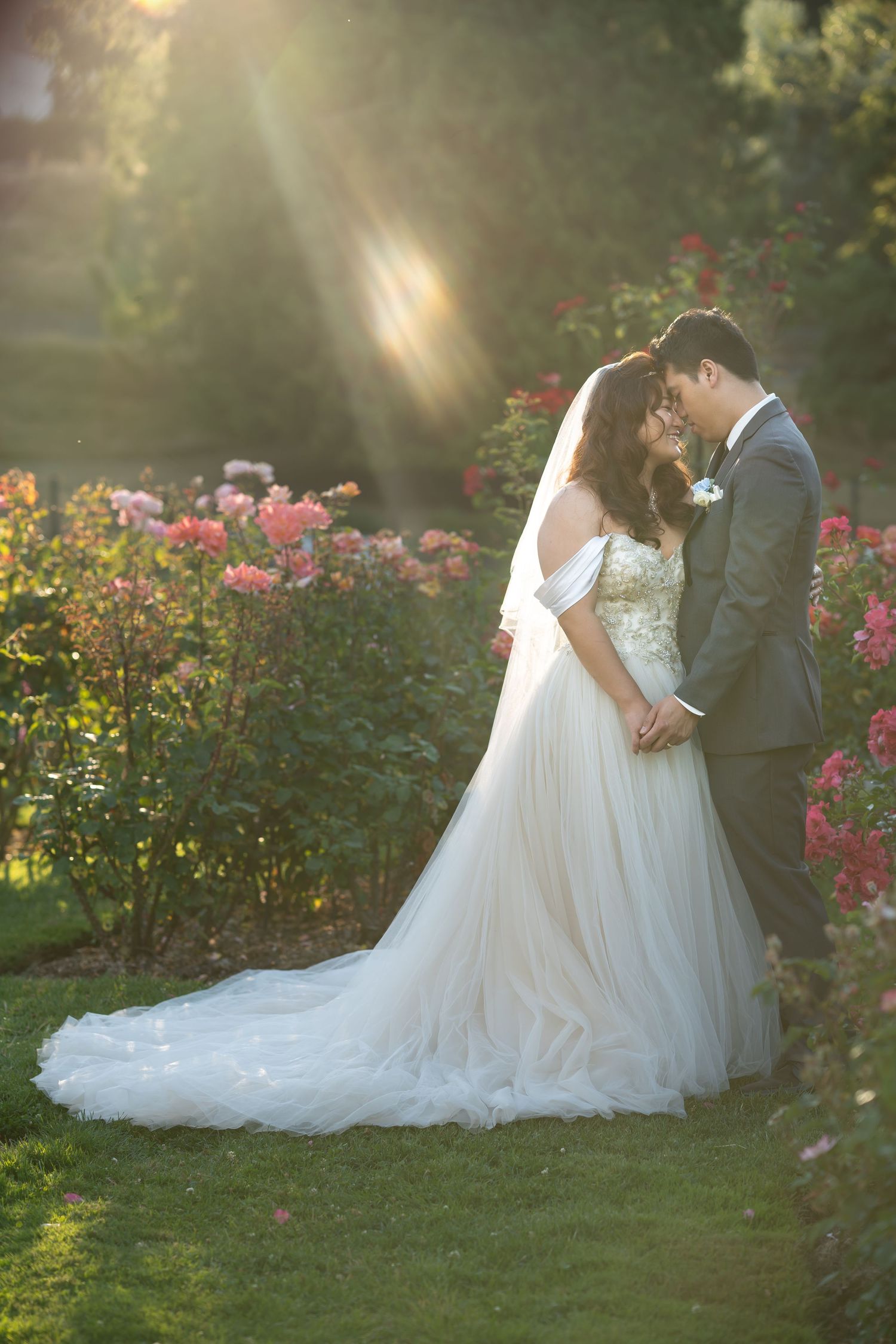 A couple shares an intimate moment in a garden with sunlight streaming through flowers.