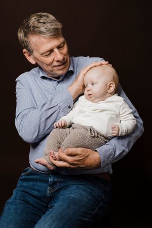 A tender moment between an adult and infant against dark background.