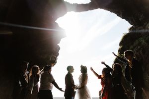 Silhouetted wedding party celebrating in a natural cave opening with bright backlighting.