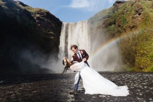 Wedding couple poses dramatically in front of majestic waterfall with rainbow.