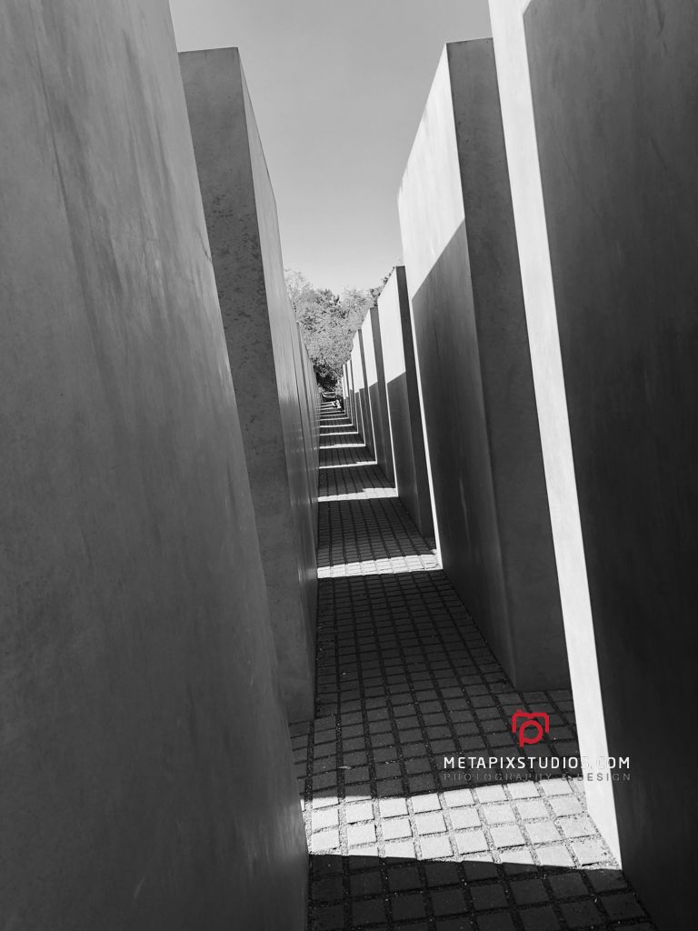 Black and white photo of a narrow pathway between tall concrete slabs at the Holocaust Memorial in Berlin.