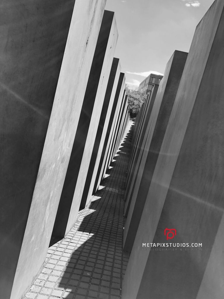 Monochrome perspective of concrete pillars casting shadows on cobblestone paths at Berlin Holocaust Memorial.