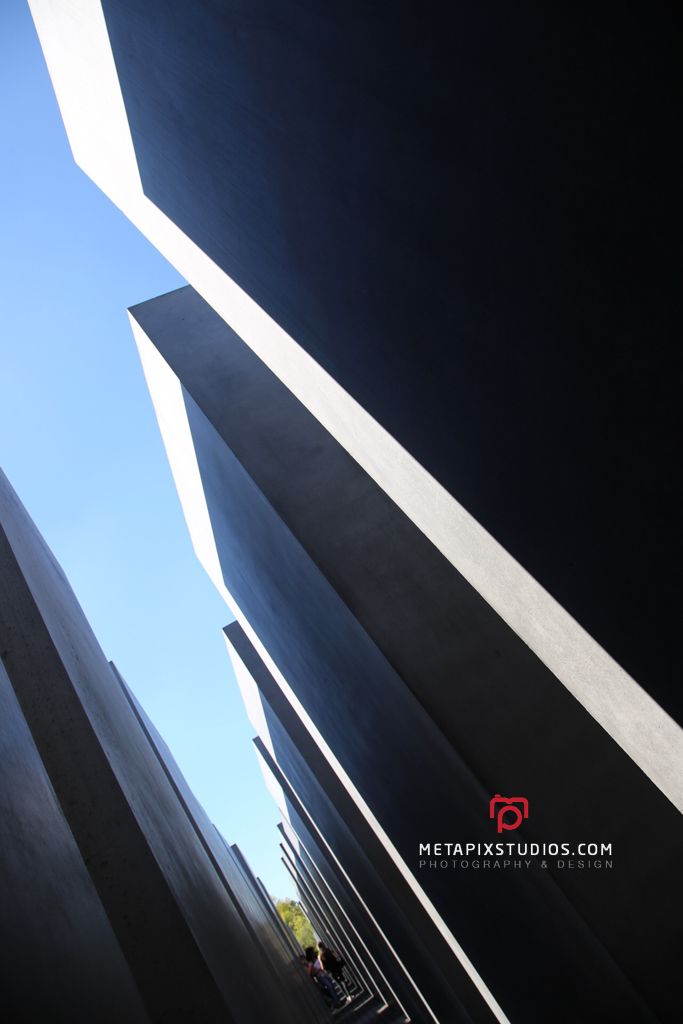 Low angle color photo of towering dark concrete pillars against a vivid blue sky at Berlin Holocaust Memorial.