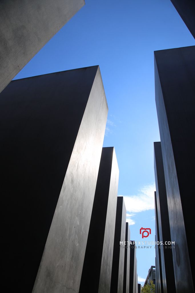 Low angle view of tall dark concrete stelae reaching toward a blue sky at the Holocaust Memorial in Berlin.