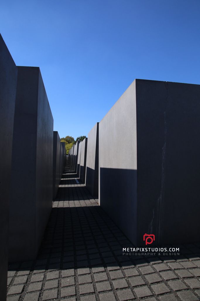 Rows of dark concrete slabs at the Holocaust Memorial in Berlin under a clear blue sky.
