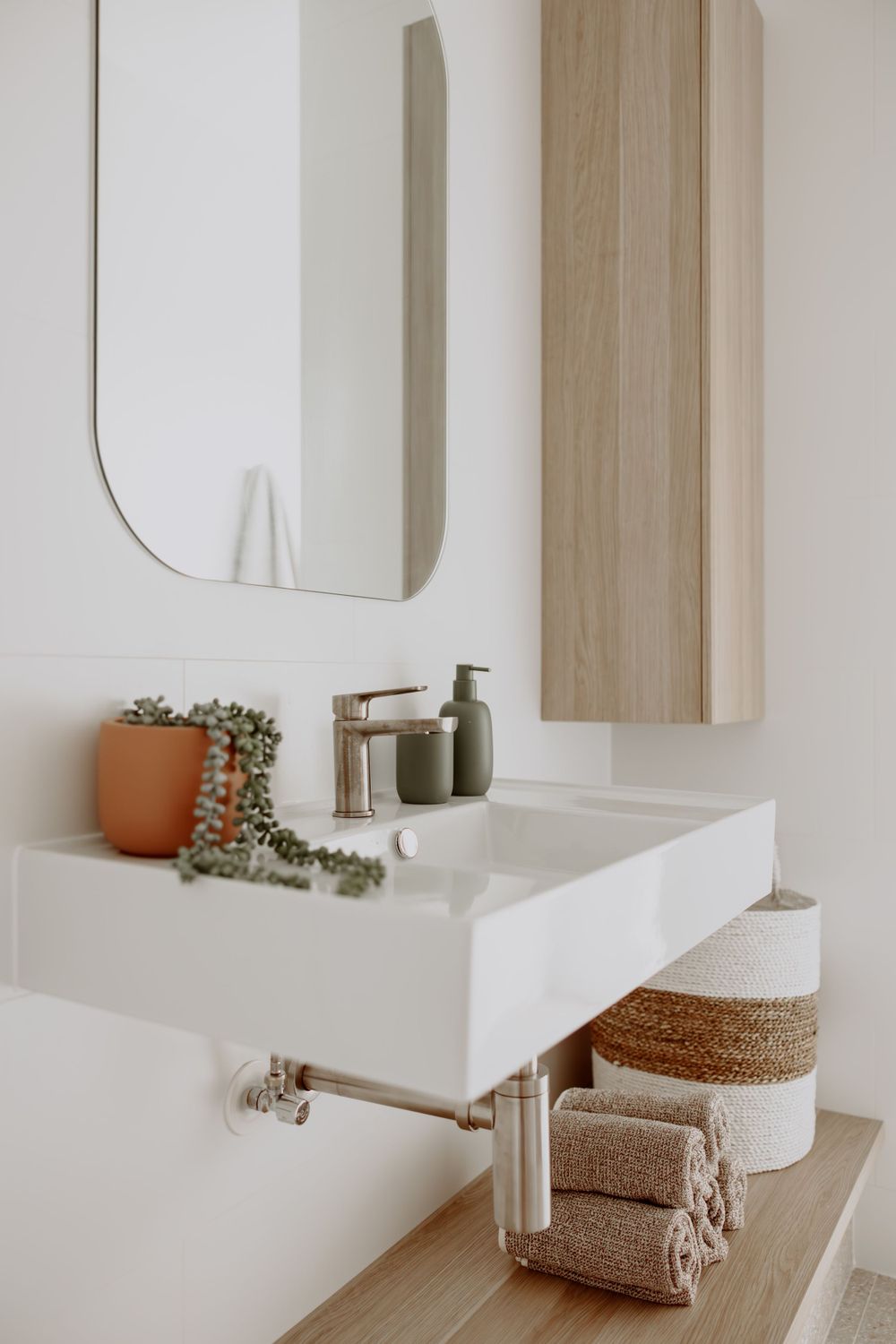 Minimalist bathroom vanity with wooden accents, white mirror, and decorative rolled towels on display.