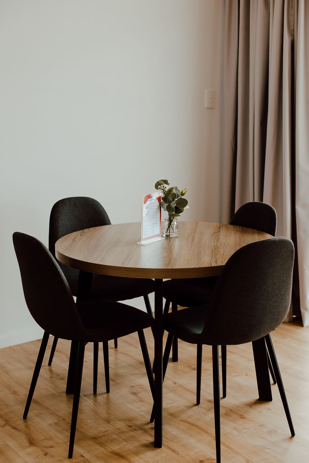 Modern dining area with round wooden table and black upholstered chairs in a minimalist setting.
