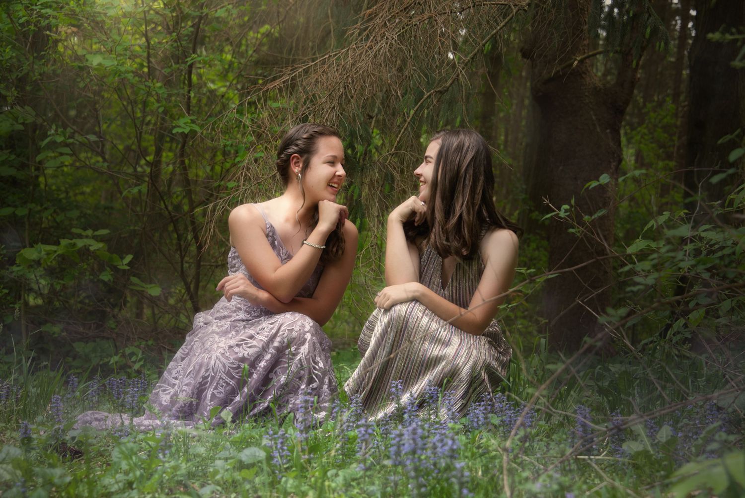 Portrait of sisters looking whimsical in the woods with purple dresses on.