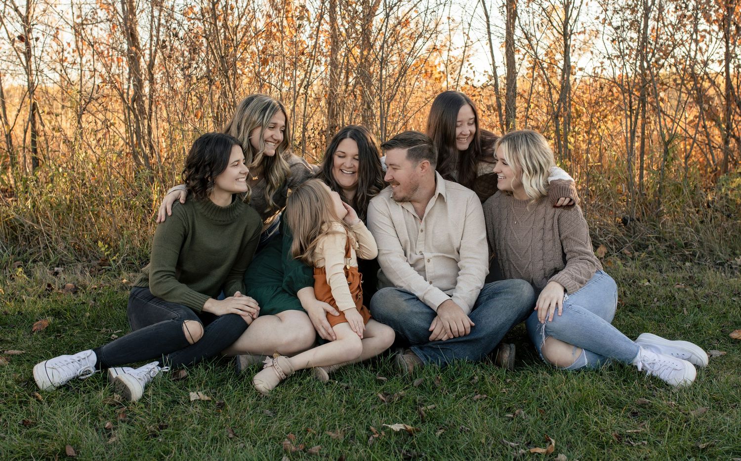 Group relaxing together on grass during outdoor autumn photo session.