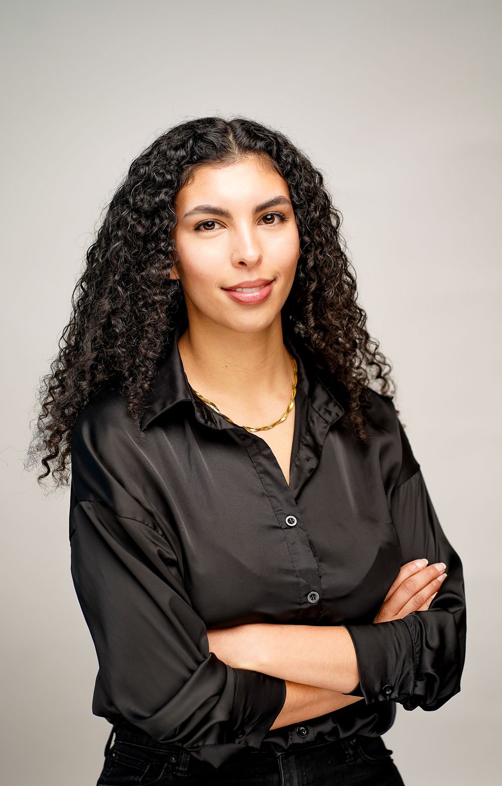 Professional studio portrait of someone in a black button-up shirt with curly hair against a gray background.