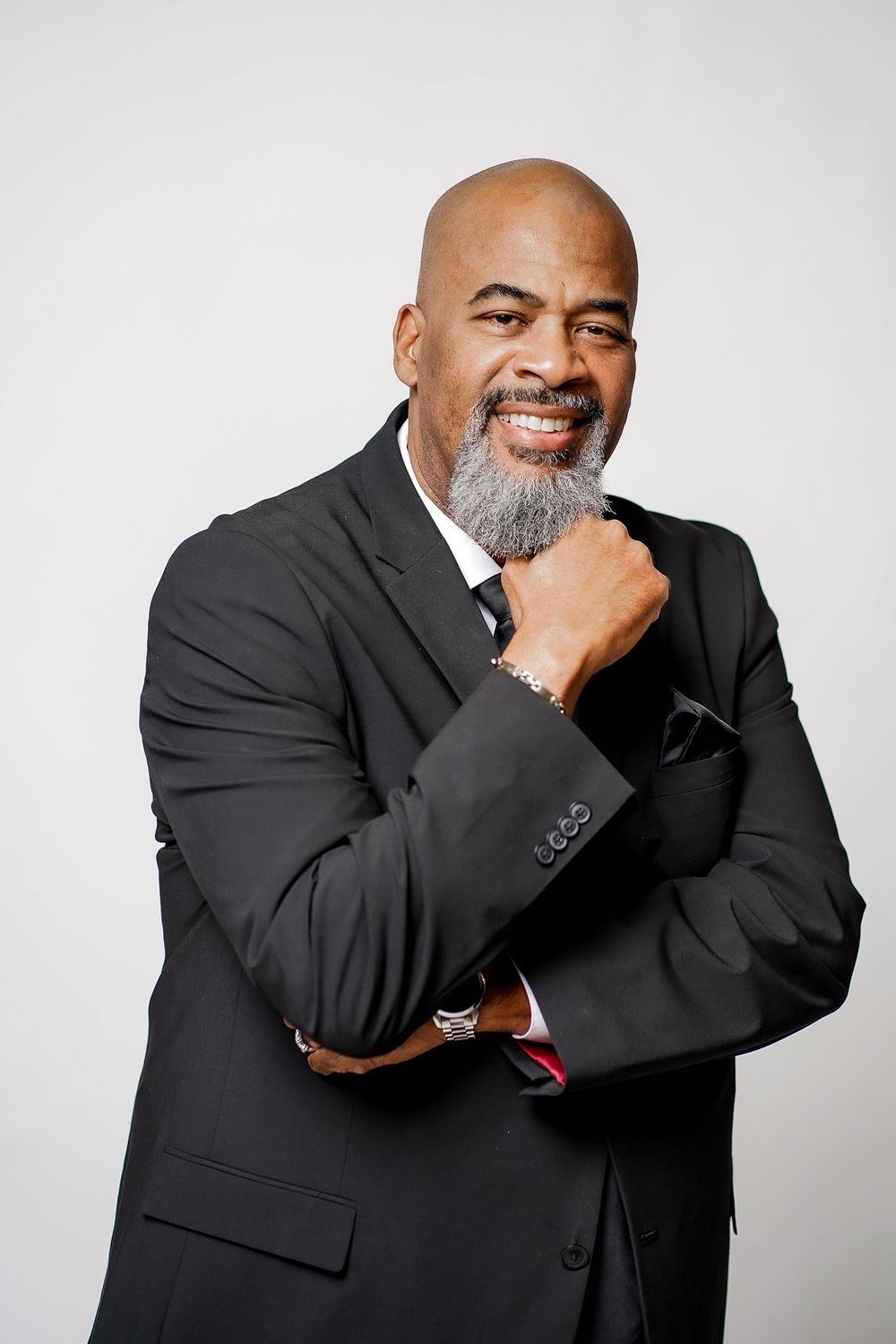 Studio portraits of person in black suit with grey beard smiling against white background.