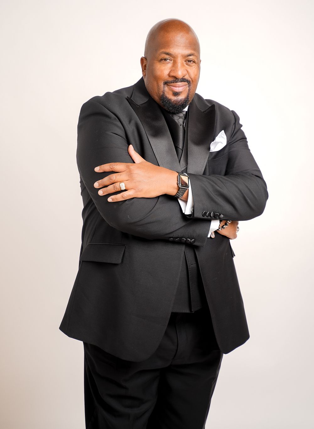 Professional in black suit jacket poses expressively against white studio background.