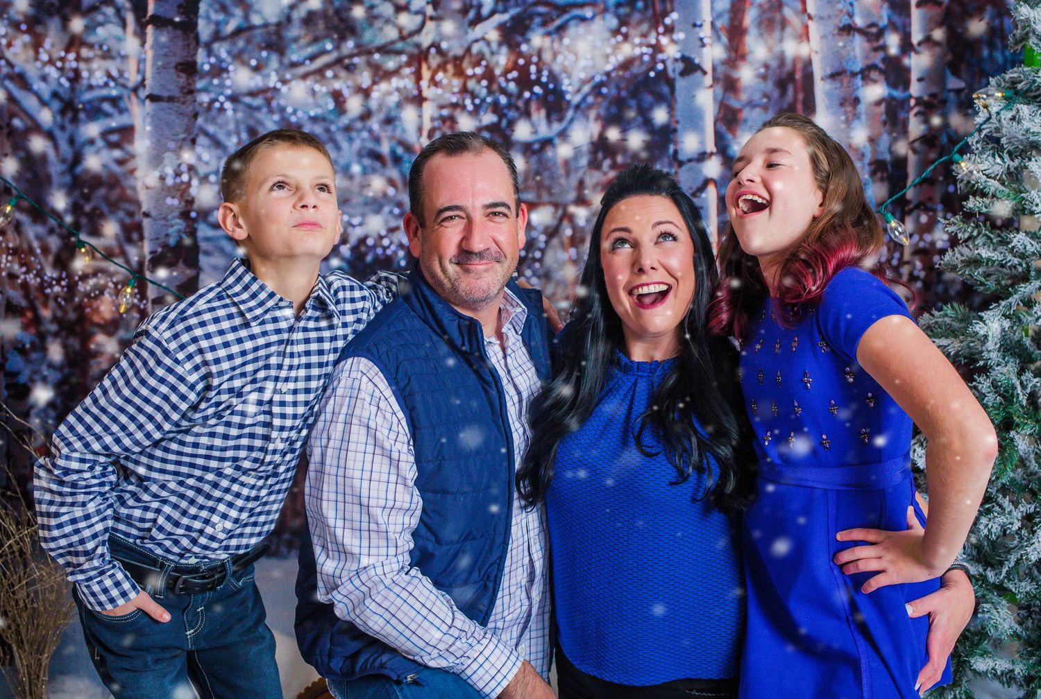 Energetic family portrait with winter backdrop showing joyful expressions and coordinated blue outfits.