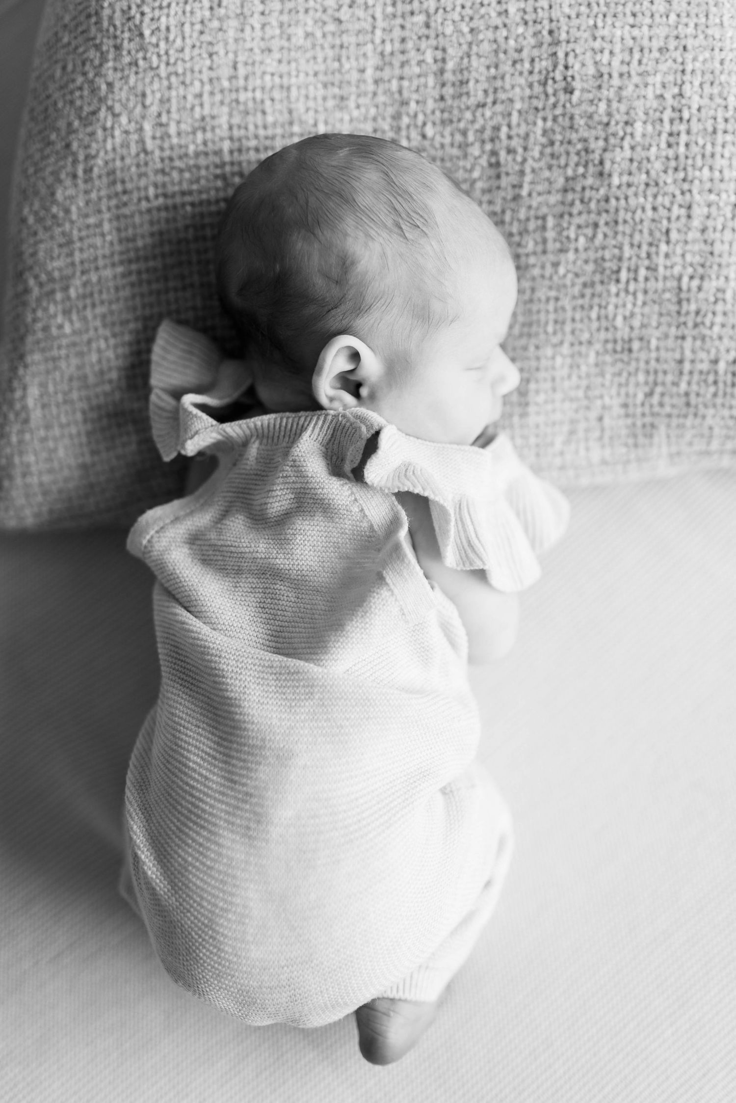 Black and white portrait of newborn baby sleeping on textured fabric.