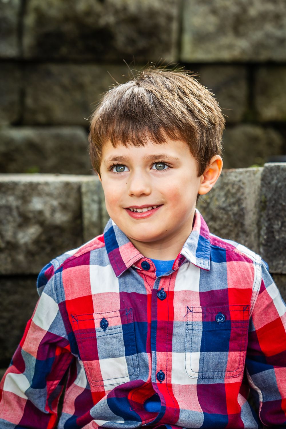 Close-up portrait against stone wall wearing red and blue plaid pattern shirt.
