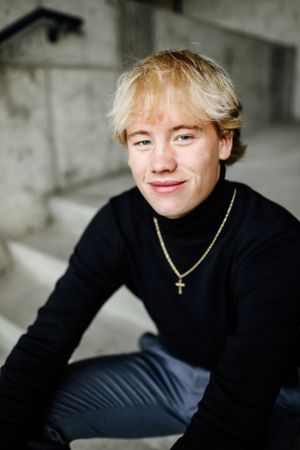 Senior in black turtleneck sweater with cross necklace against gray background.
