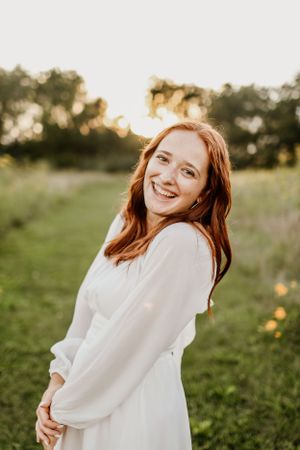 Portrait of someone in white dress smiling in sunlit field at golden hour.