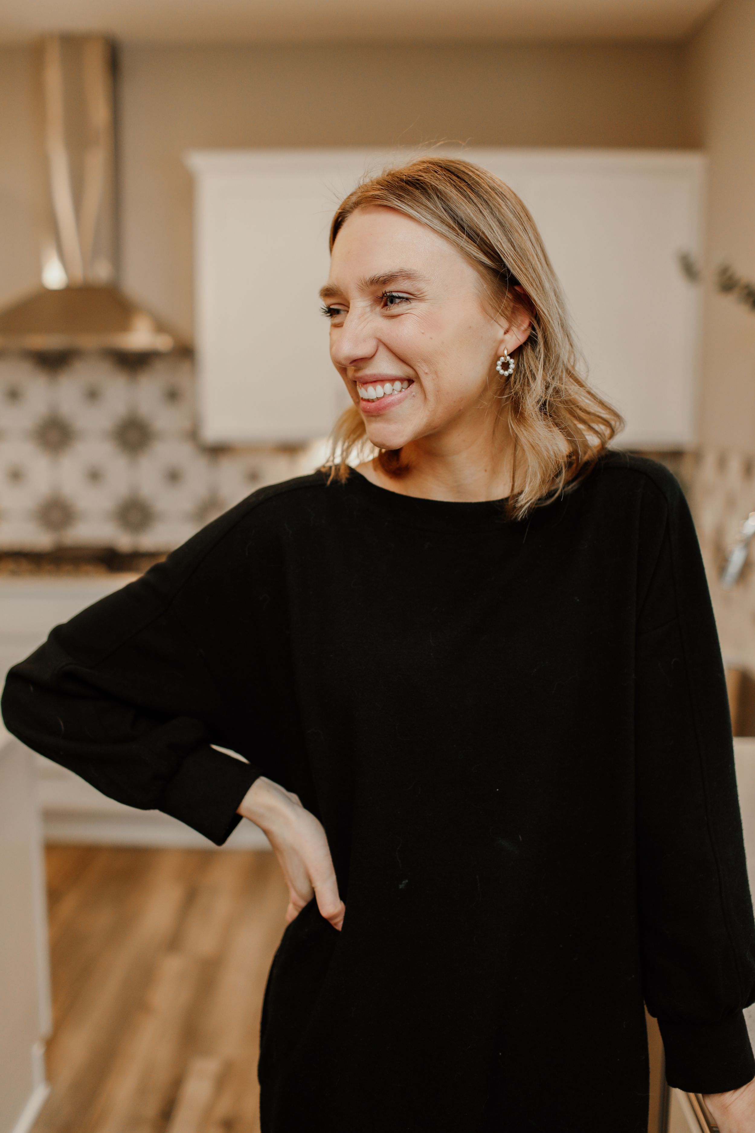Woman in black sweater smiling warmly in modern kitchen setting.