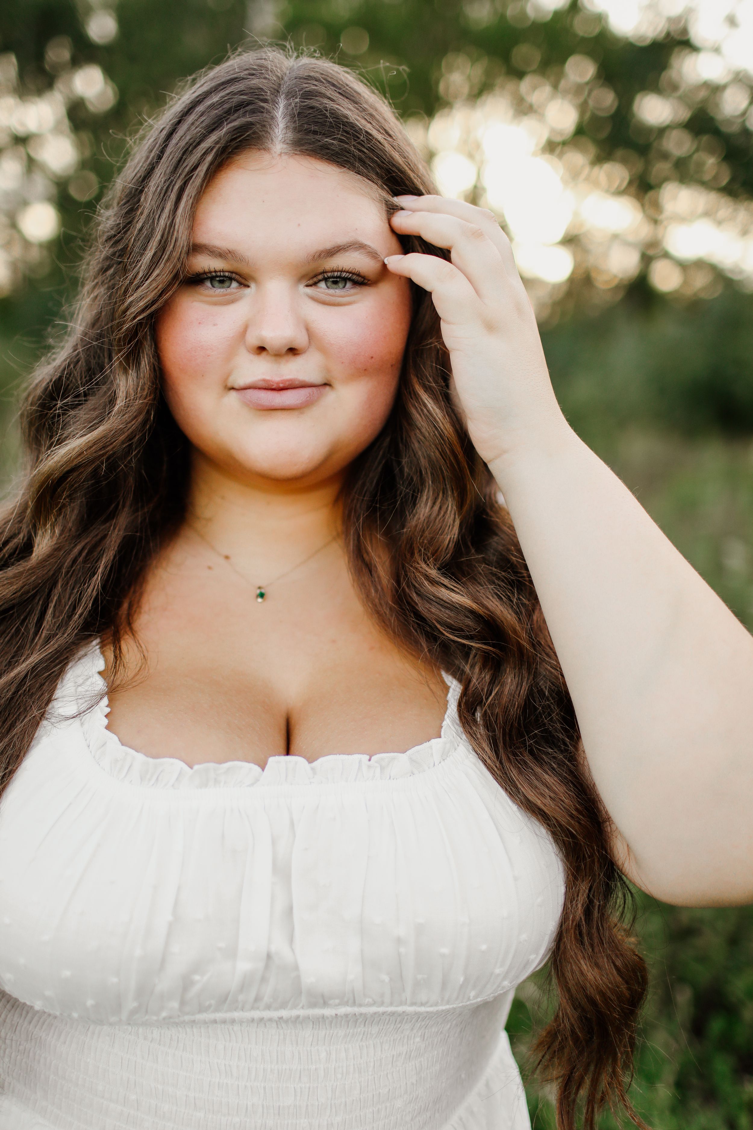 Young woman in white dress poses outdoors during golden hour photoshoot.