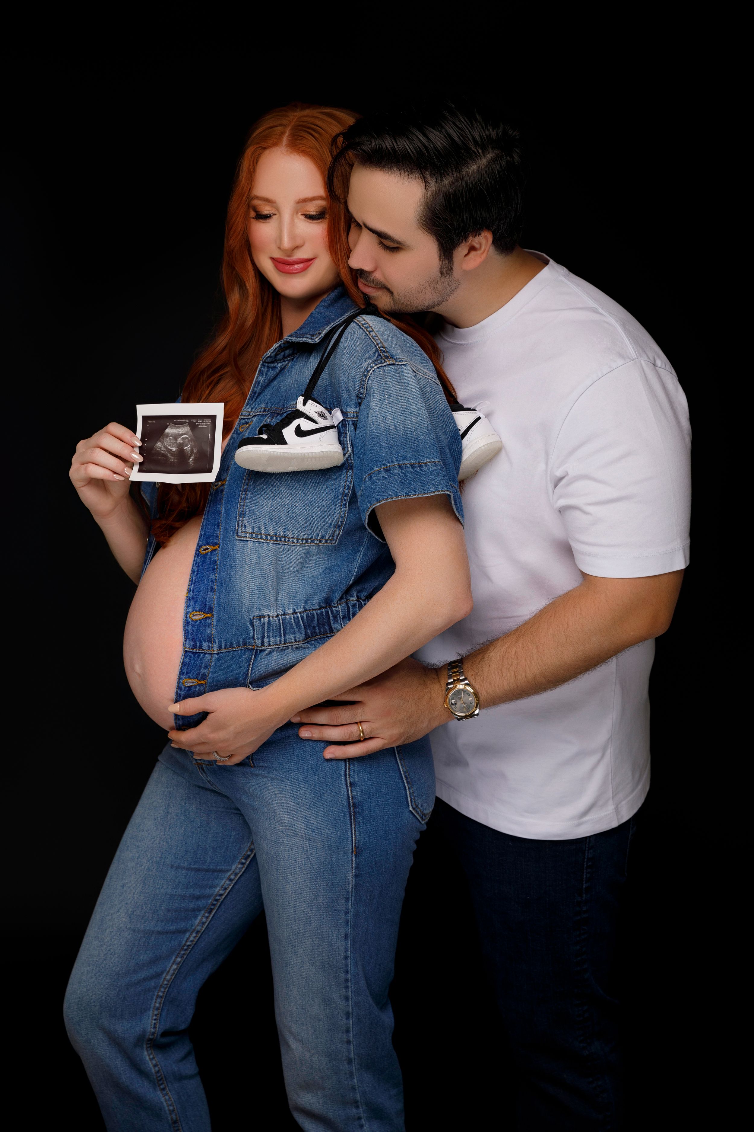 San Diego studio maternity session, a redhead model wearing a denim jumpsuit with her spouse, by Daryana Orange.