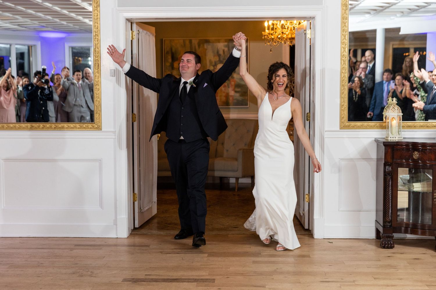 Couple makes grand entrance into reception hall with raised arms in celebration.