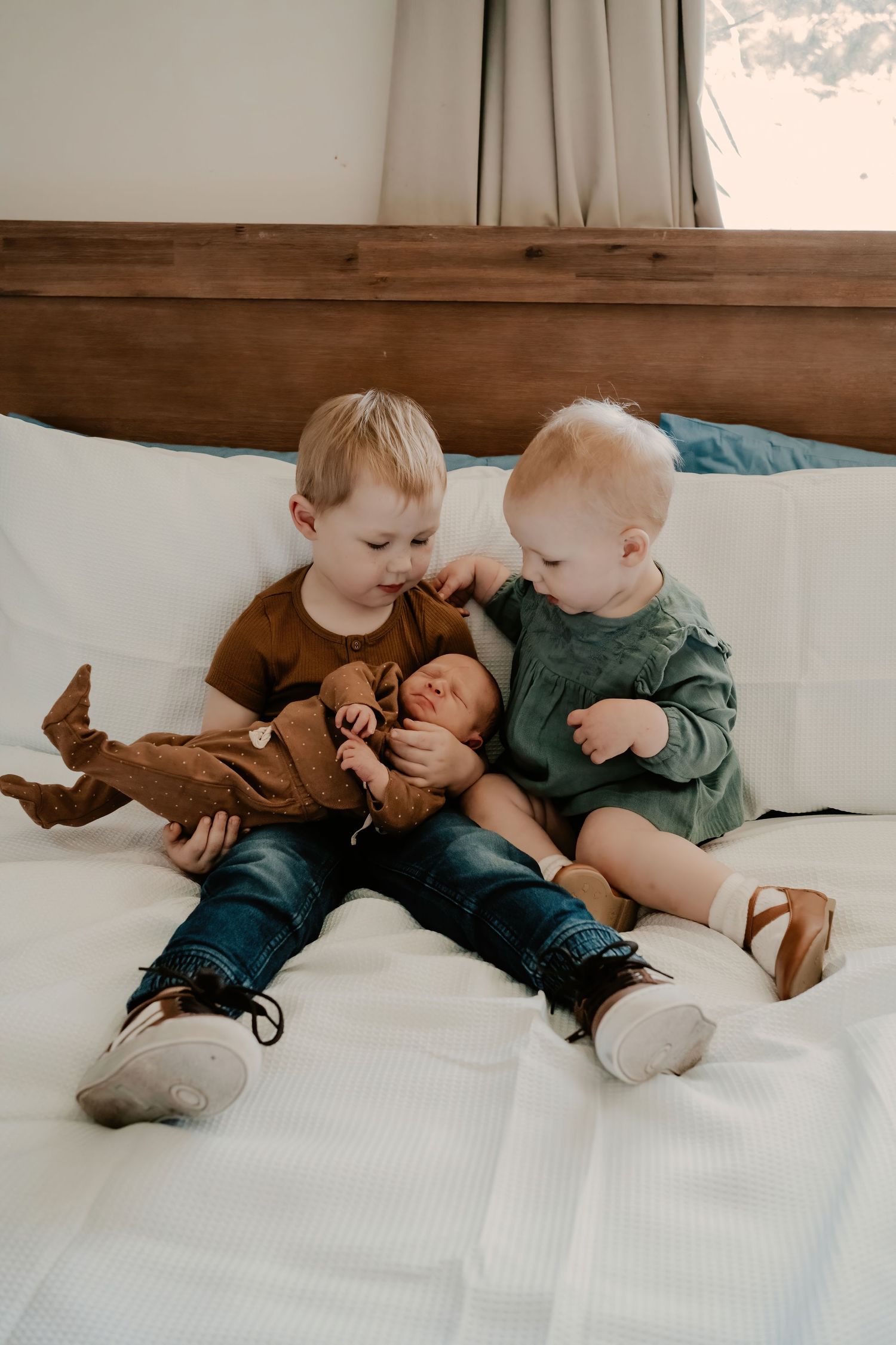 Young siblings in casual attire lying on a white bed together sharing a sweet moment.