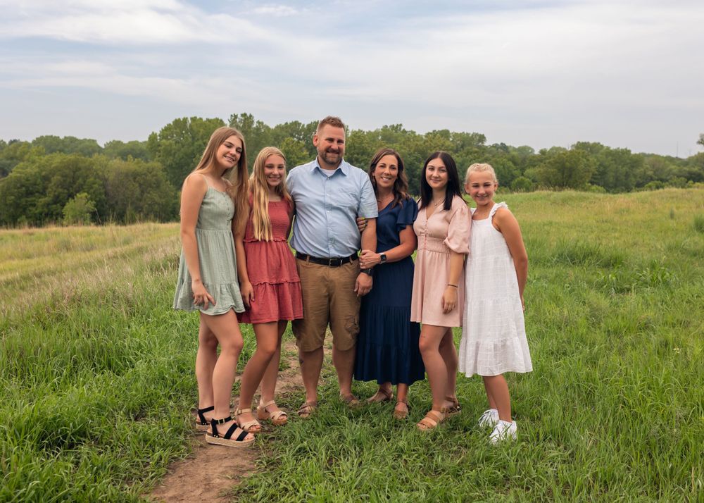 Group portrait of family members standing together in a sunny meadow.