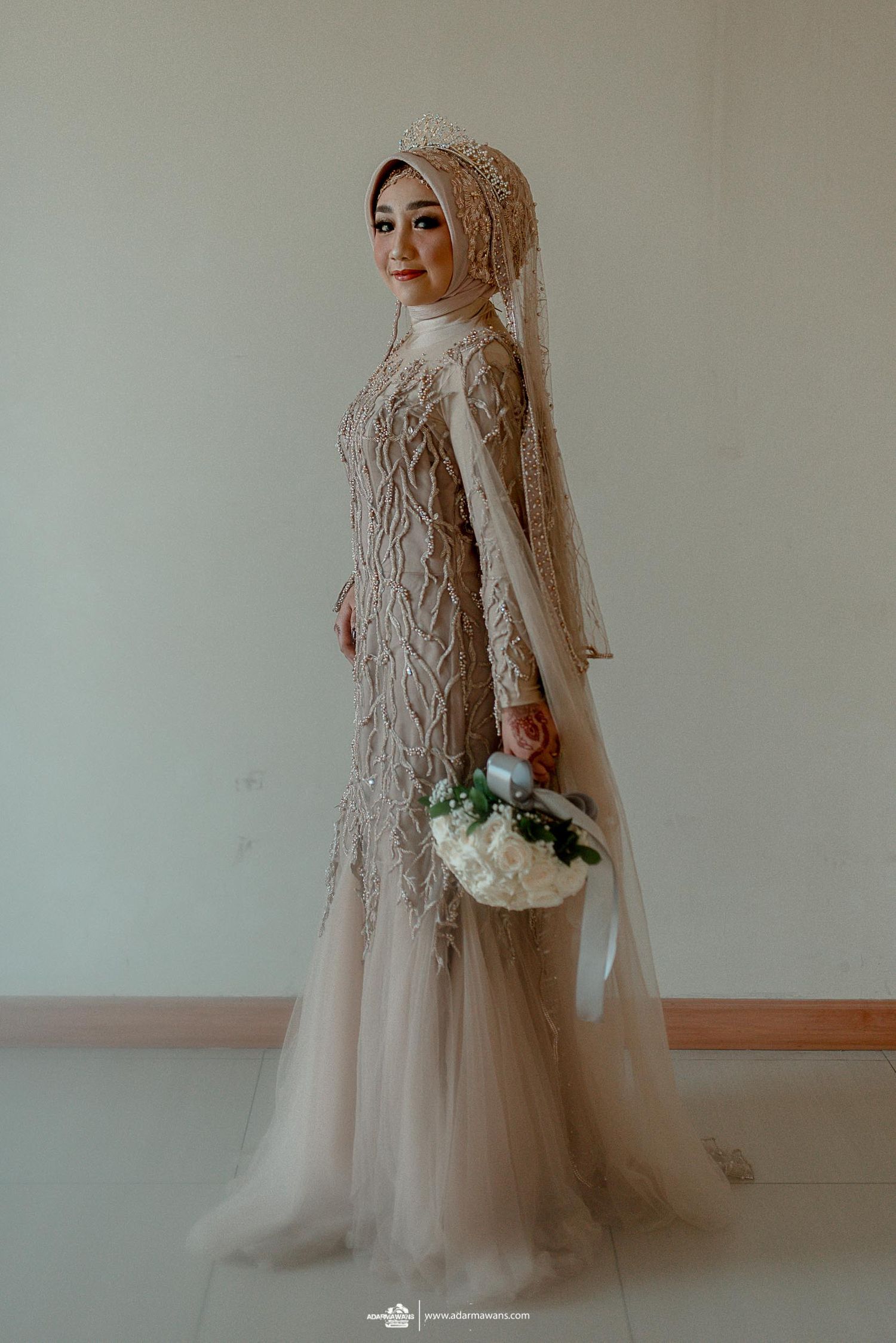 A bride poses in an elegant beige lace wedding gown with floral bouquet.