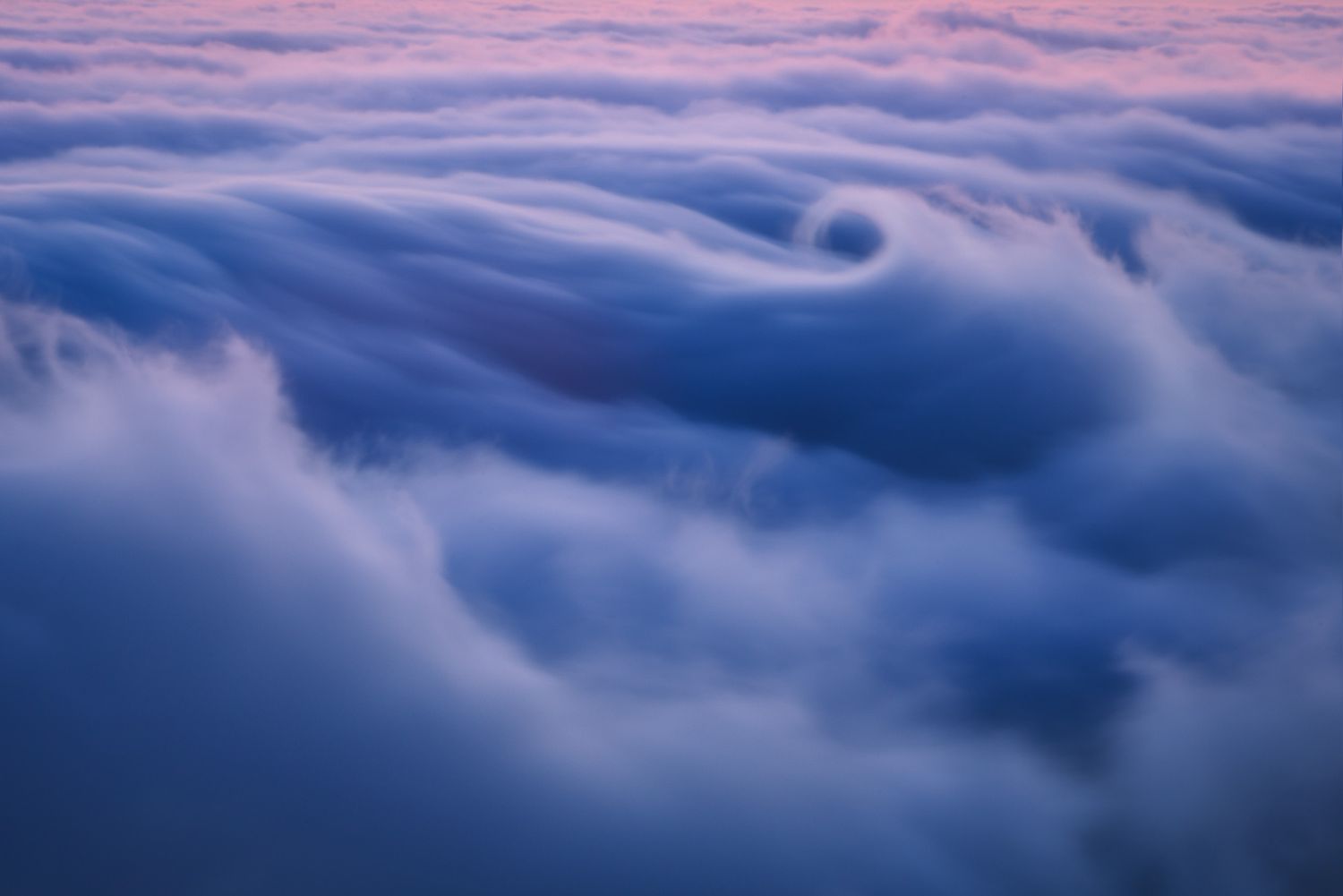 Smooth waves of blue clouds roll across the sky in an ethereal pattern at twilight.