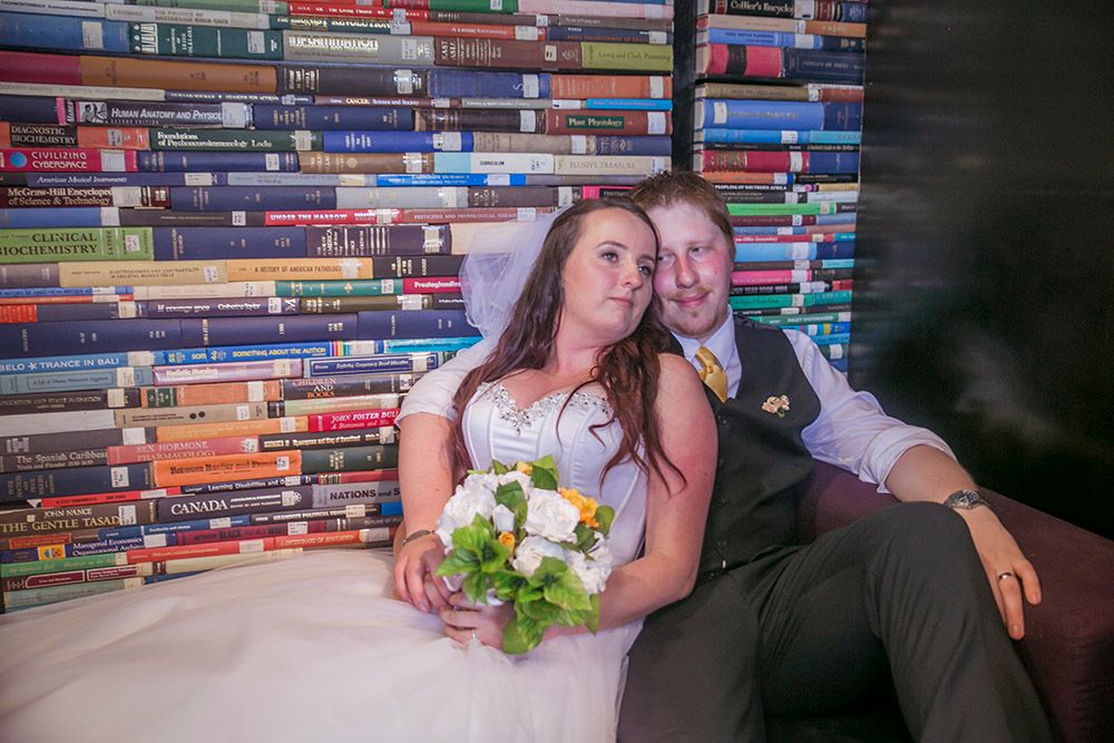 Wedding couple poses against unique backdrop of colorful bookshelves in library setting.