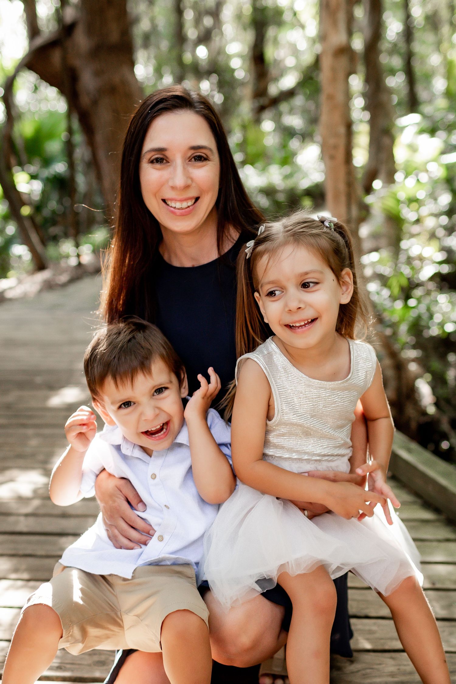 Happy family portrait on a rustic wooden boardwalk surrounded by tropical foliage.