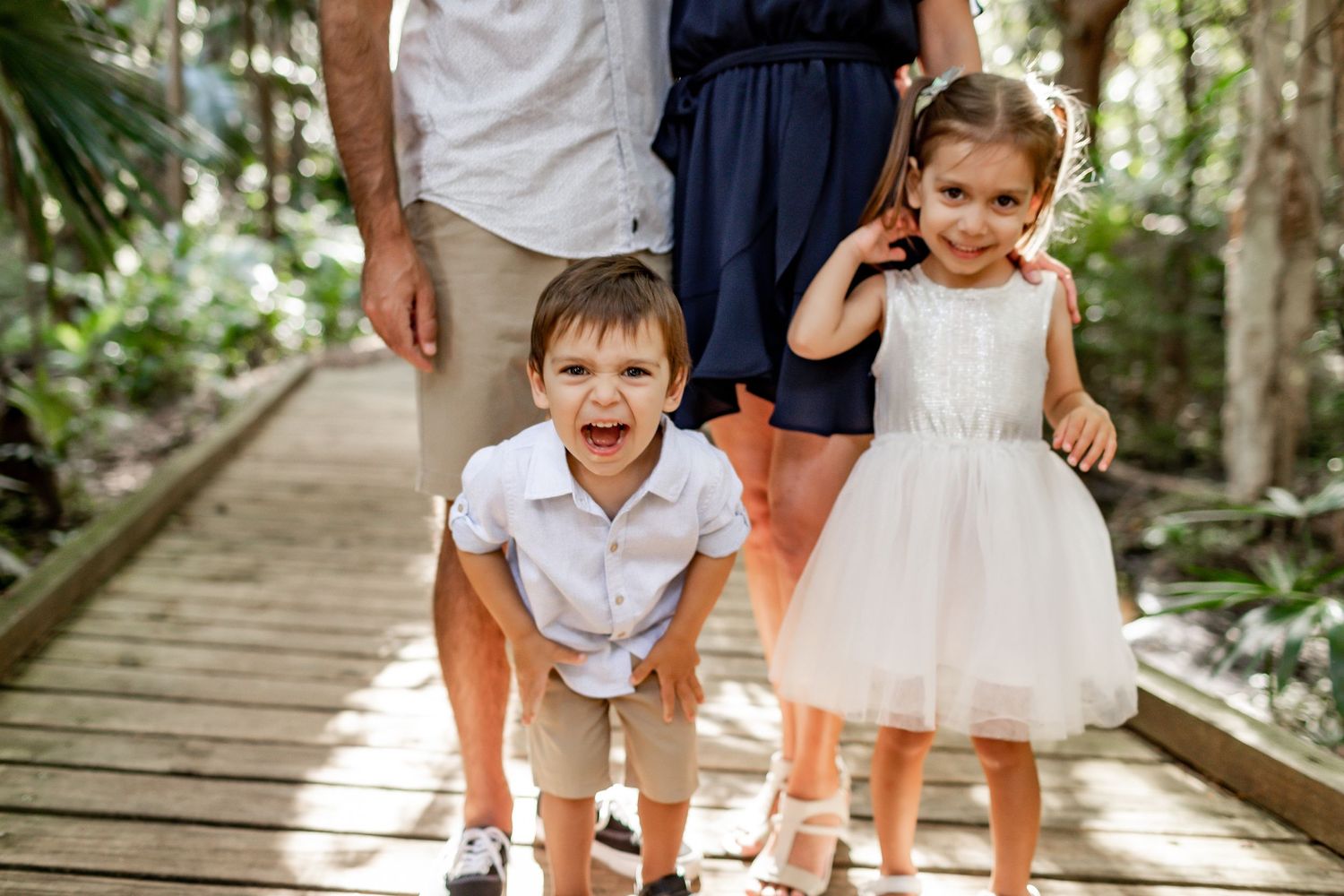 Playful children posing on wooden boardwalk in tropical forest setting.