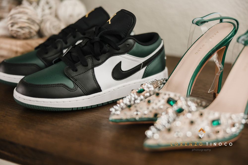 Green and black Nike sneakers paired with crystal-studded heels on wooden surface.