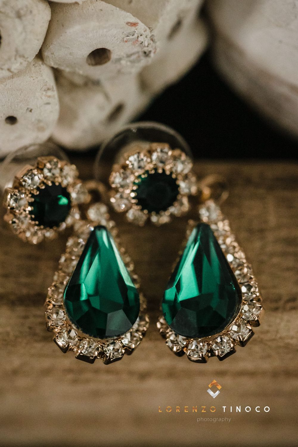 Elegant emerald teardrop earrings adorned with crystal rhinestones on a rustic wooden surface.