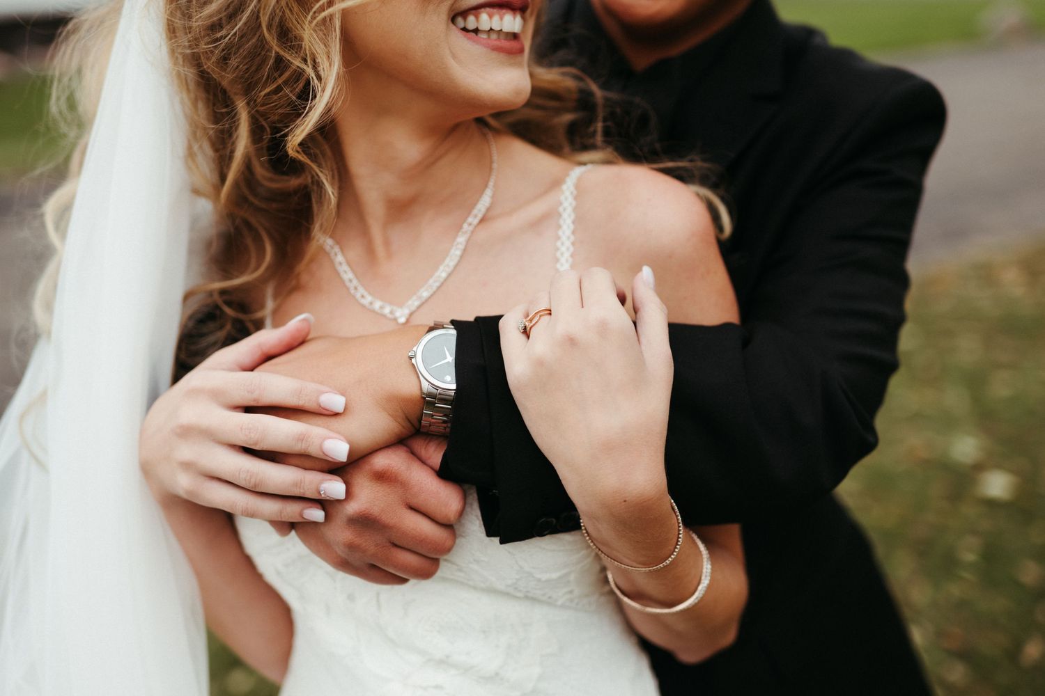 Close-up of wedding rings and jewelry with couple embracing.