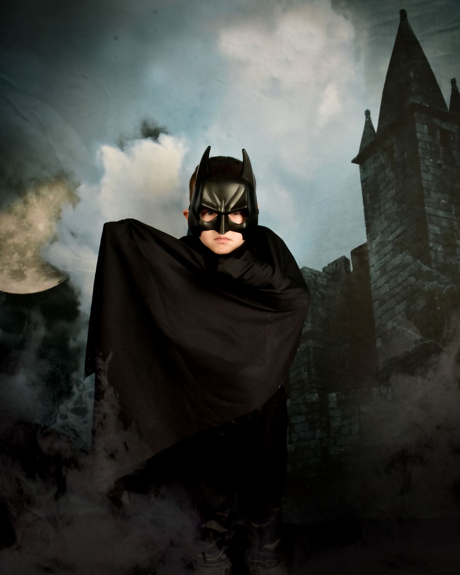 Dramatic Batman costume photo against gothic castle backdrop with fog effects.
