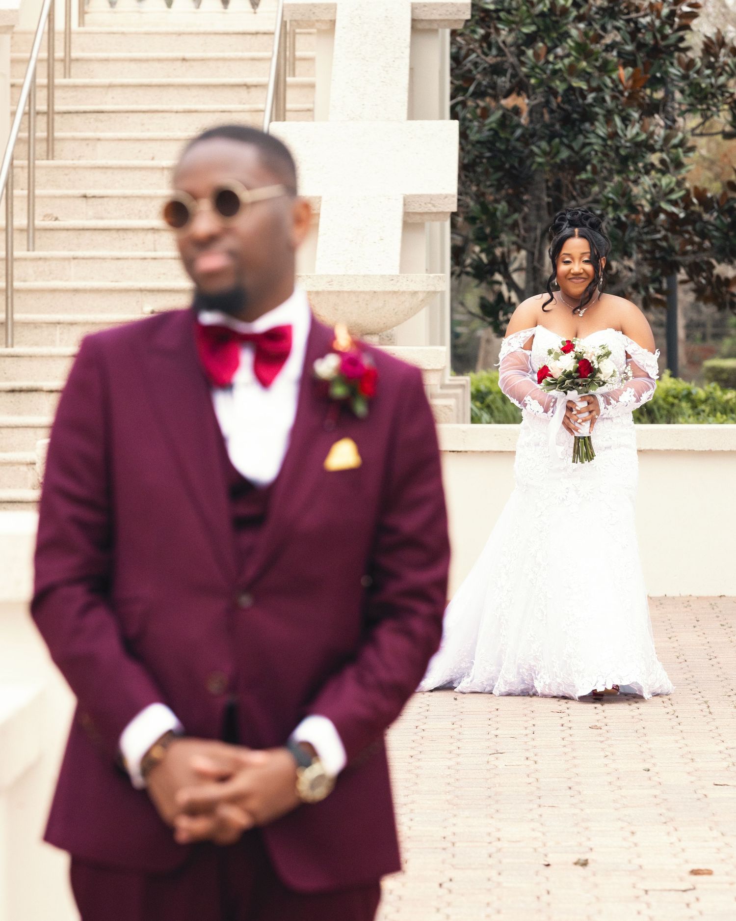 Wedding couple in burgundy suit and white dress posing separately on stone steps.