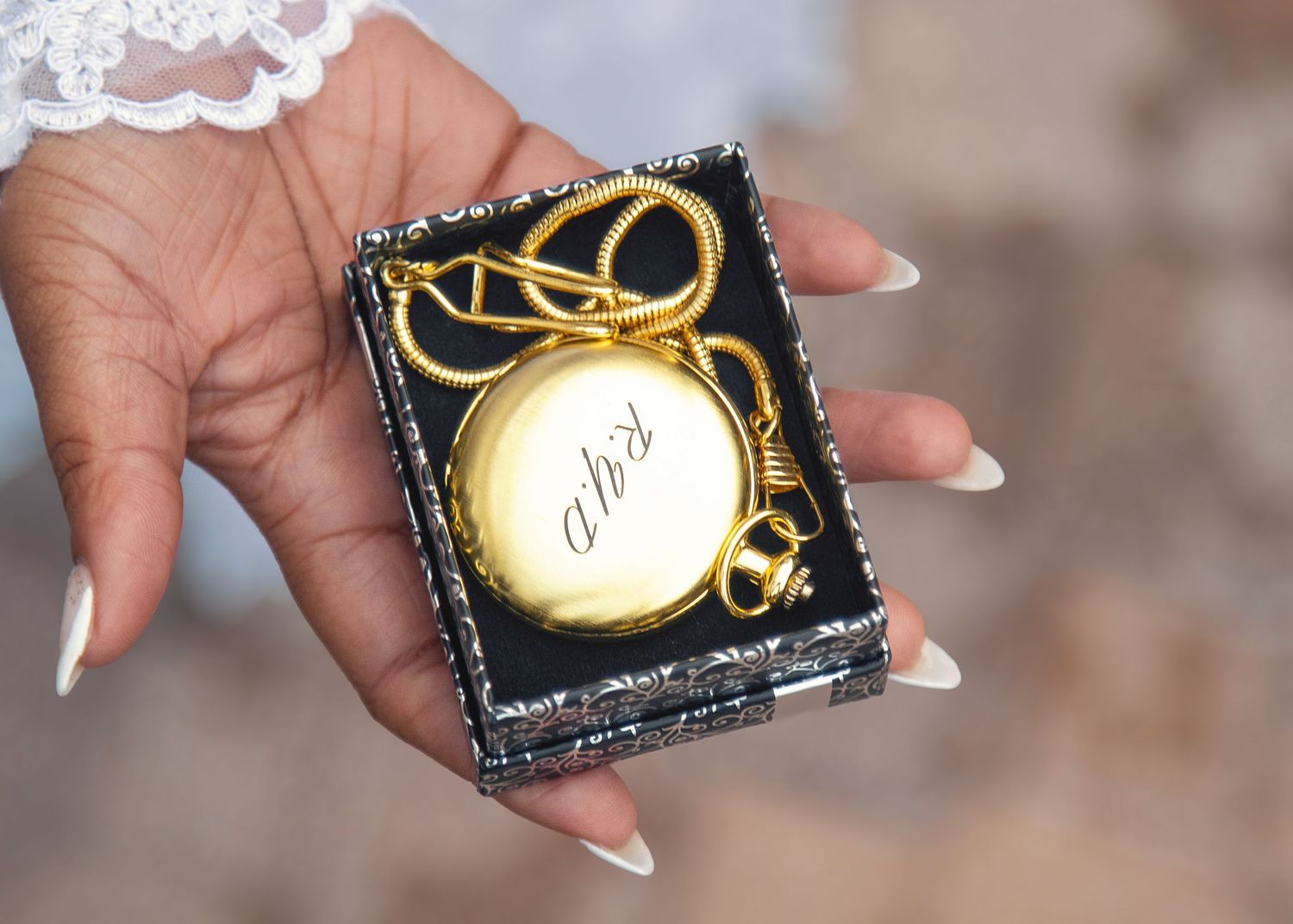 Close up of a hand holding a small black box with gold ornament.