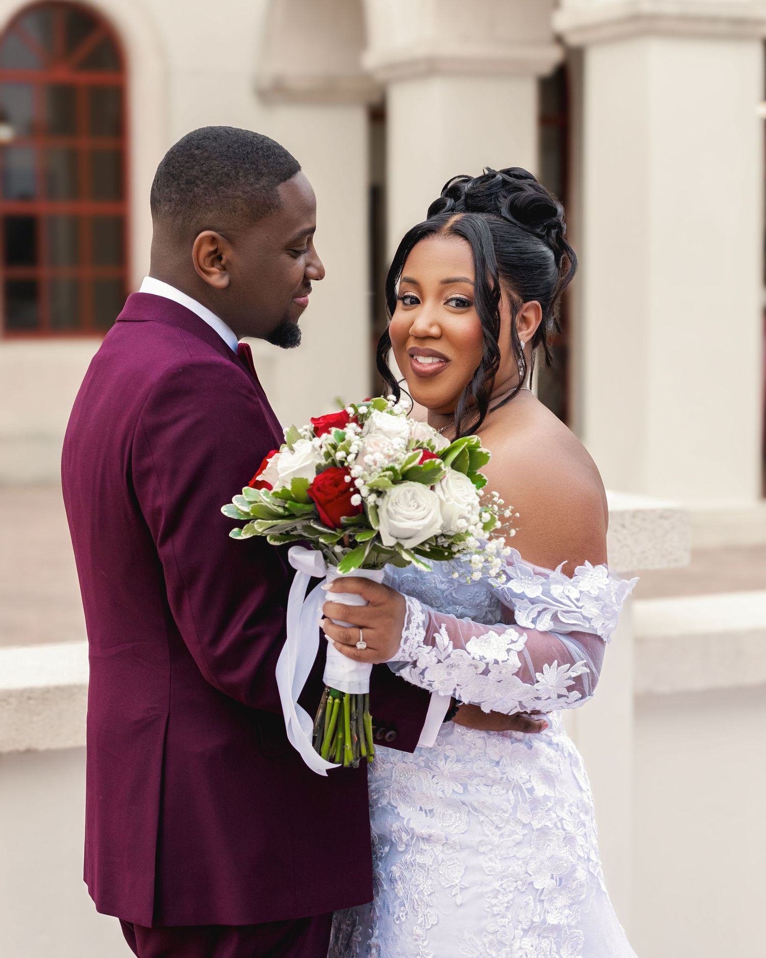 A romantic wedding moment between newlyweds, with the bride holding a white flower bouquet.