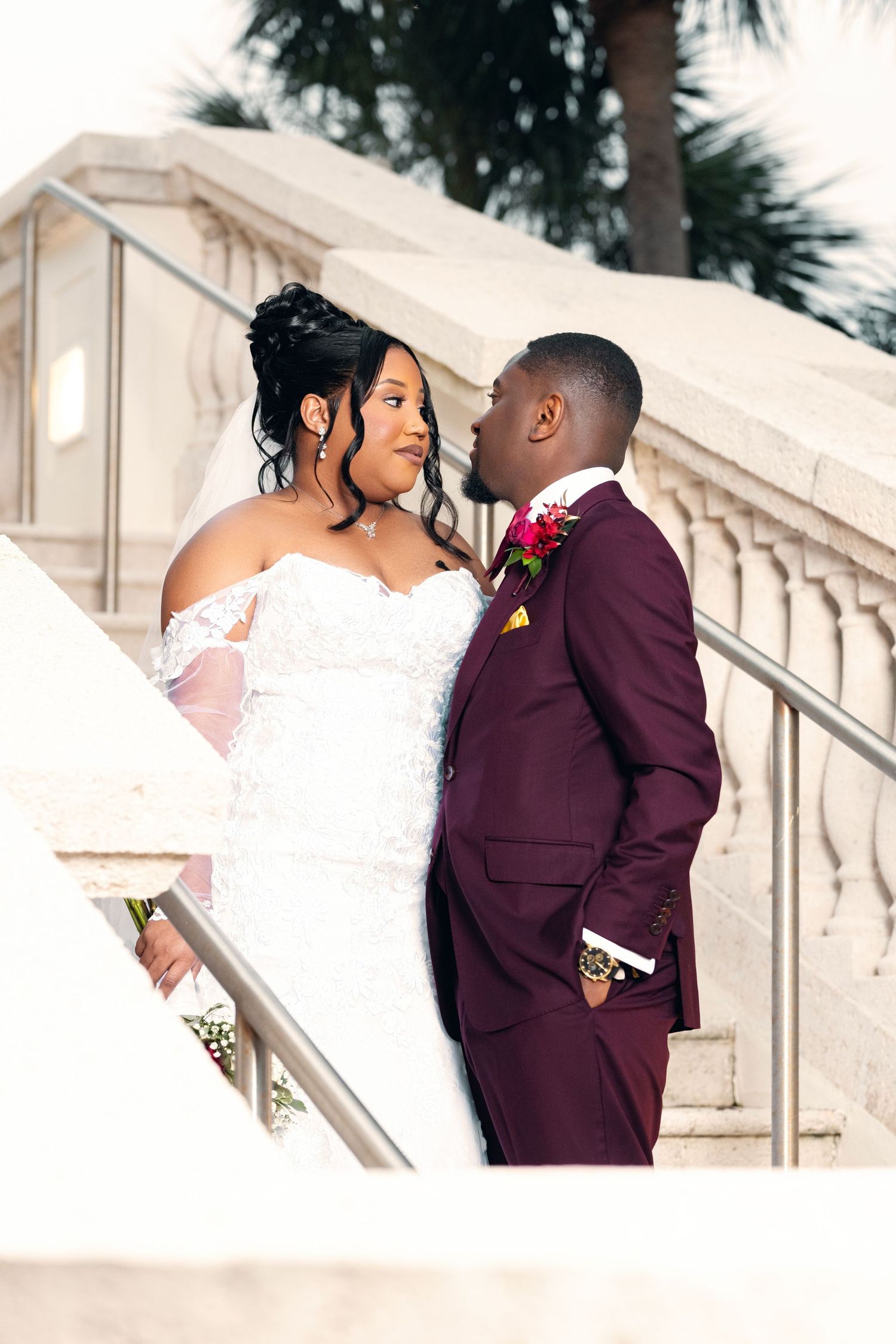 A romantic wedding moment on marble stairs with burgundy suit and white lace dress.