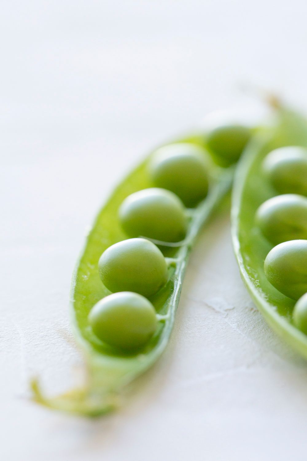 Fresh green peas lined up perfectly inside an opened pod on a white surface.