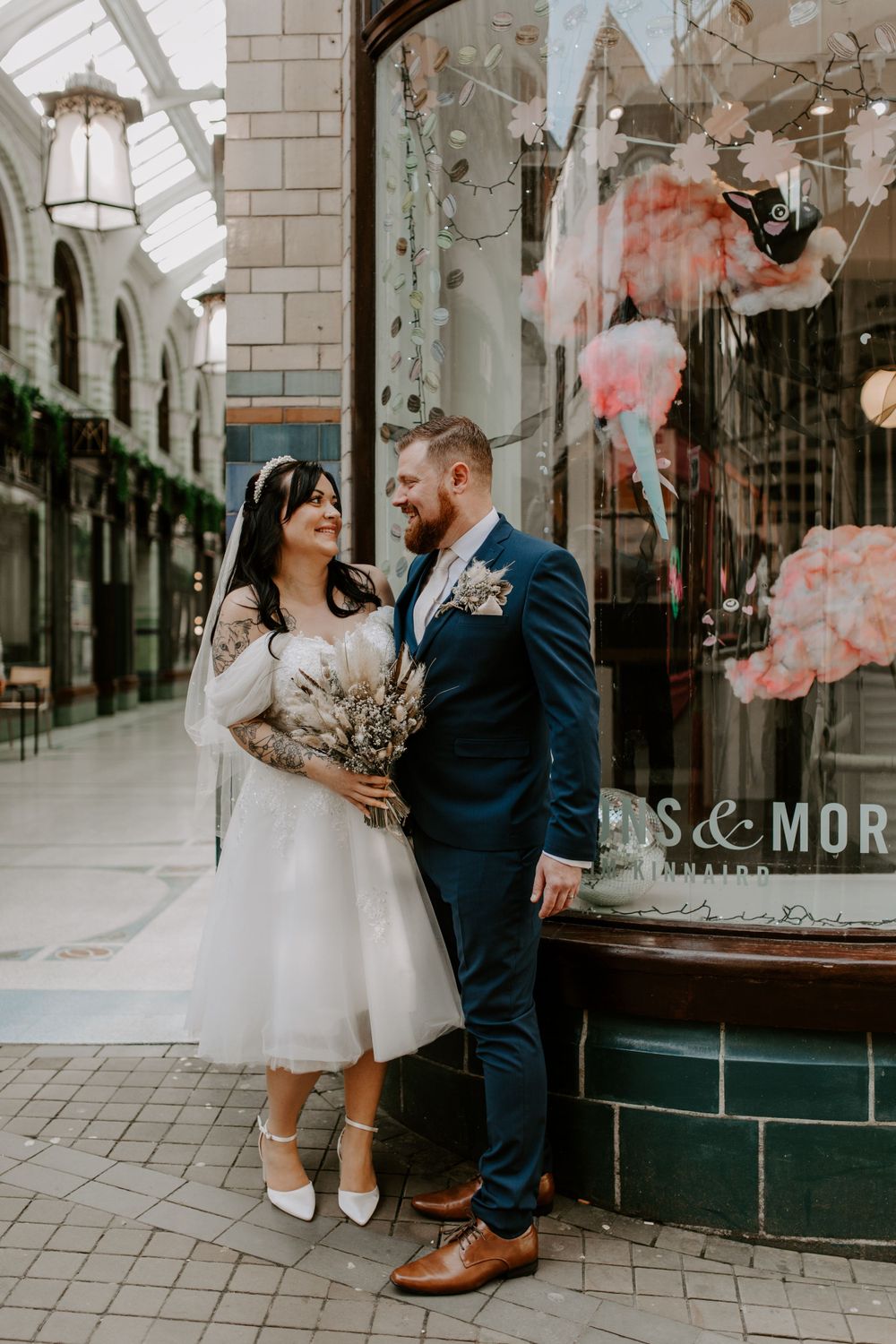 bride and groom standing outside a macaron shop in the city centre. they are looking at each other and smiling.