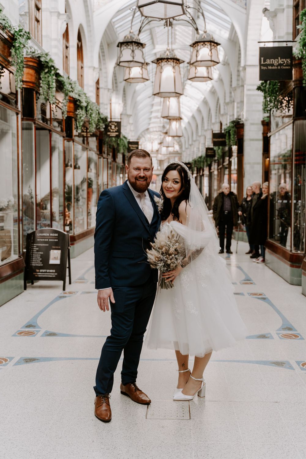 bride and groom standing in a shopping mall in the city centre. they are looking at each other and smiling.