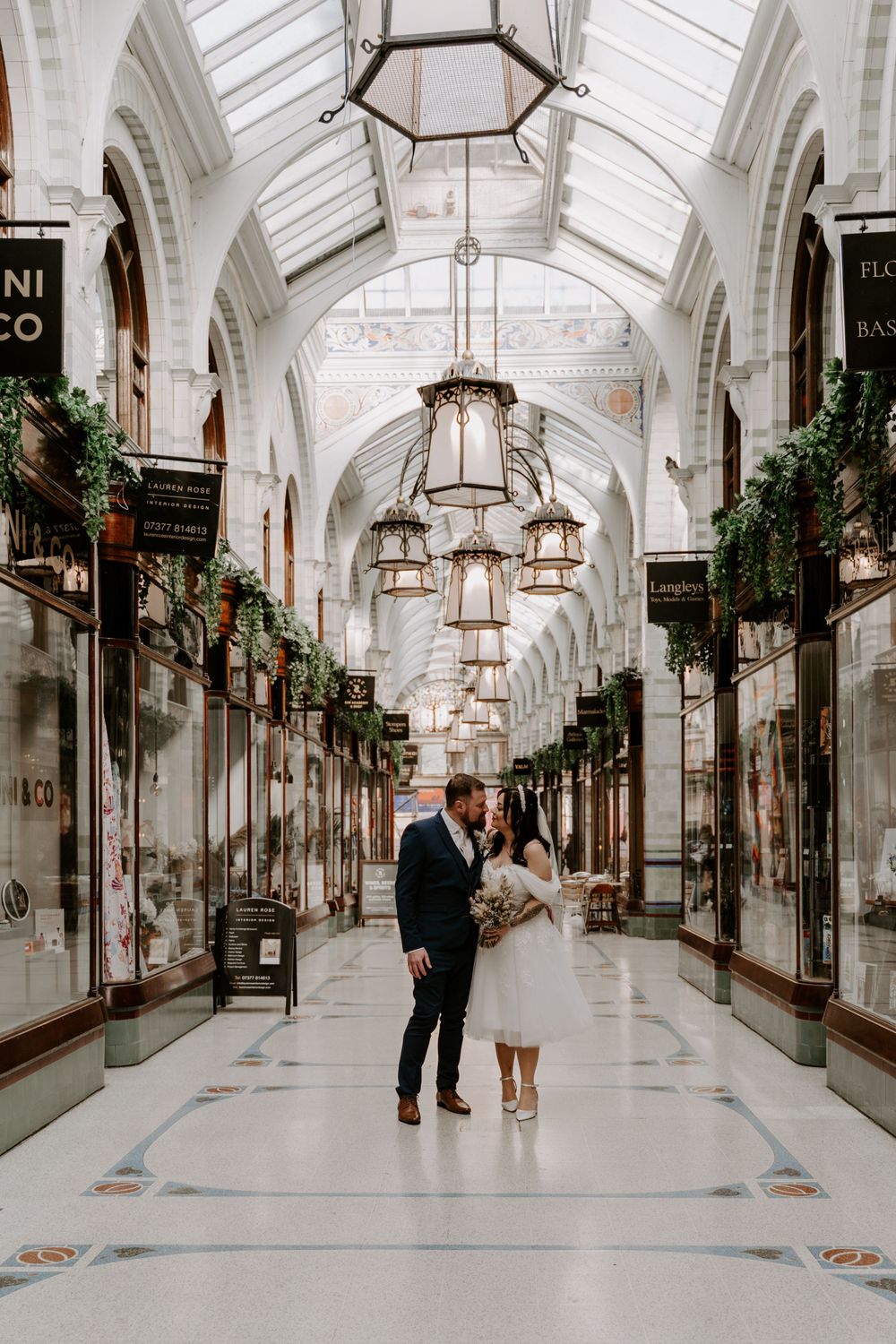 bride and groom standing in a shopping mall in the city centre. they are kissing.g.