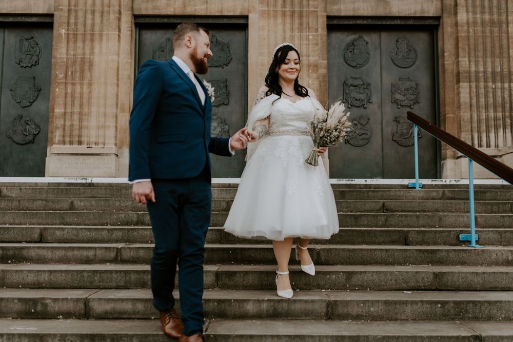 groom holding his brides hand and leading her down some steps in the city centre.