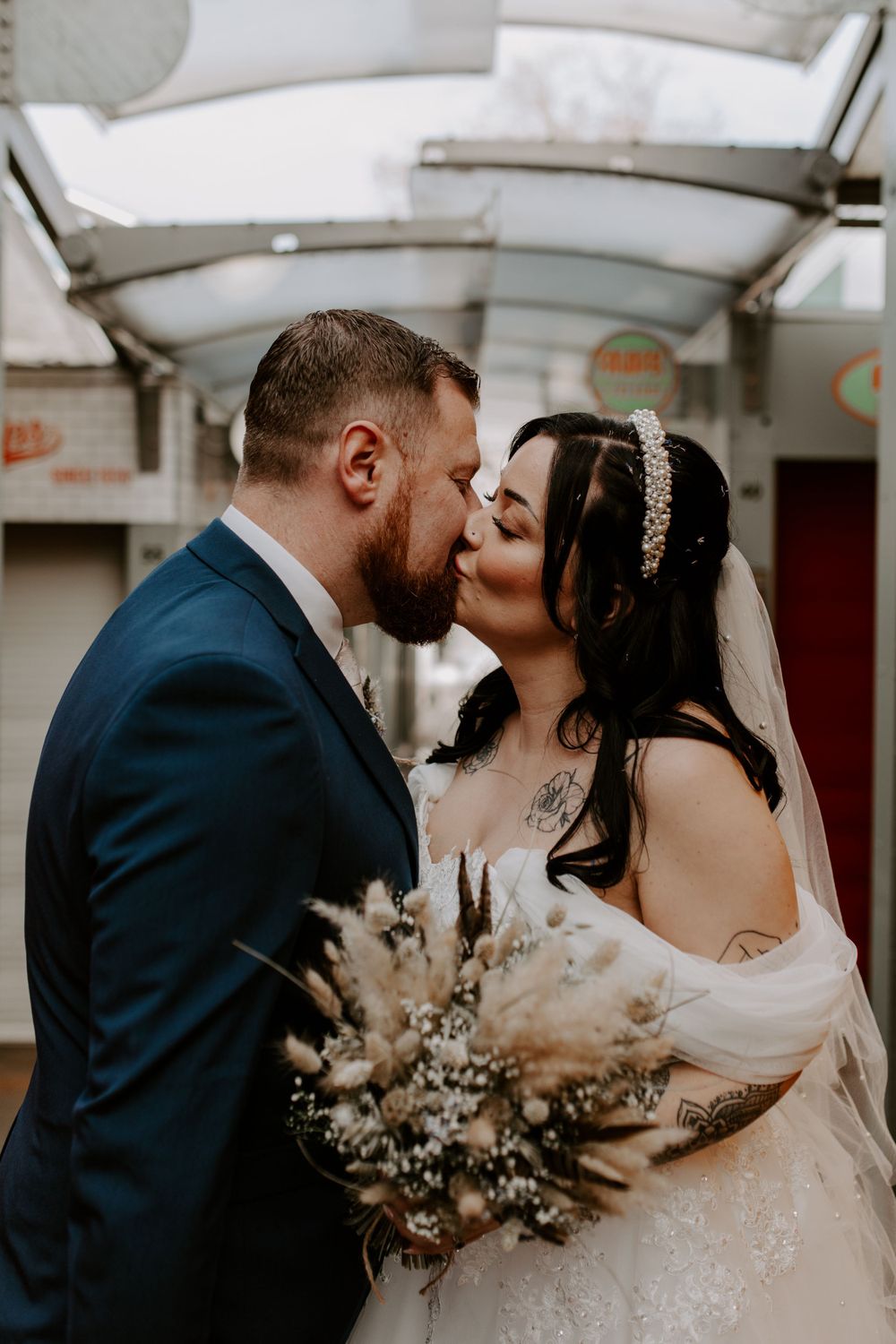 bride and groom kissing. She is holding a dried flower bouquet.