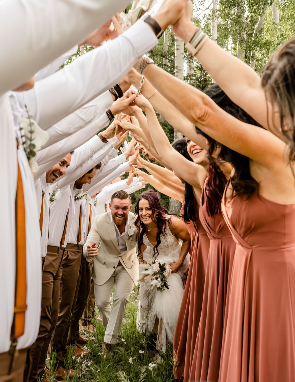 Wedding party in dusty rose dresses and light suits celebrating outdoors.
