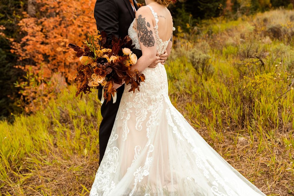 Autumn wedding photoshoot with couple in white dress and suit against orange foliage.