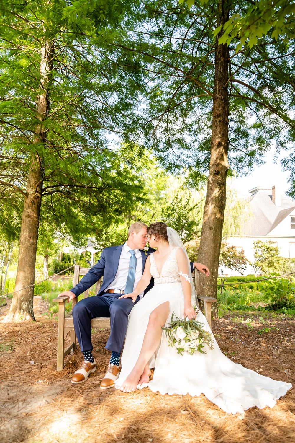 Wedding couple sitting together under green trees on a sunny afternoon.