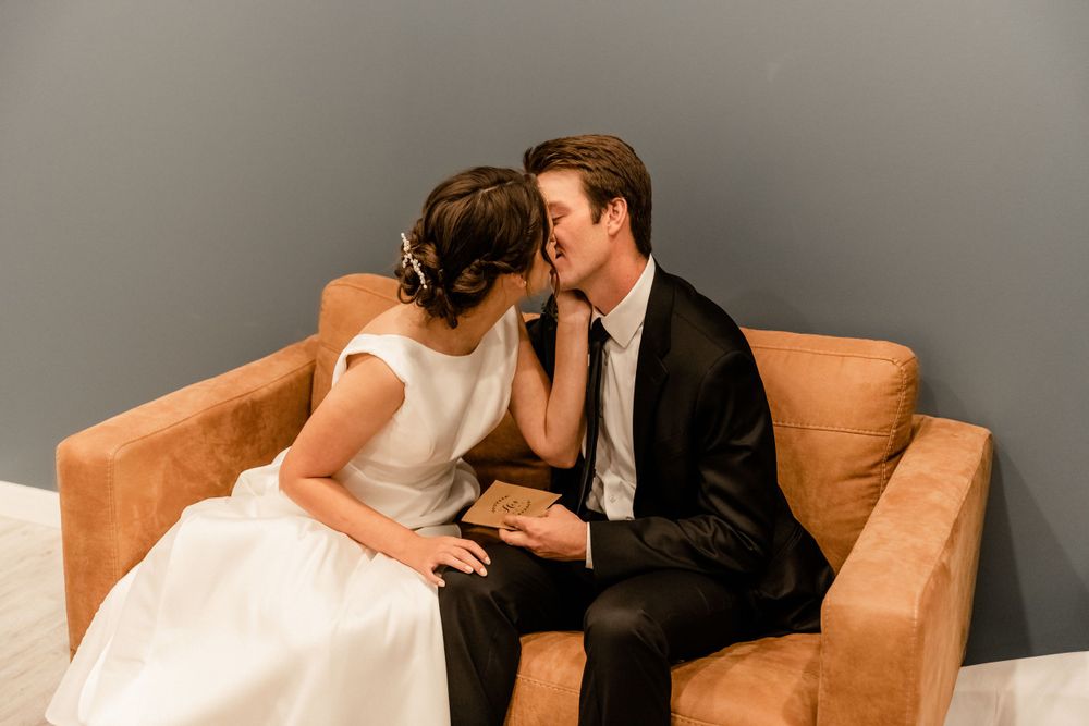 Romantic wedding couple sharing intimate moments on a beige couch.